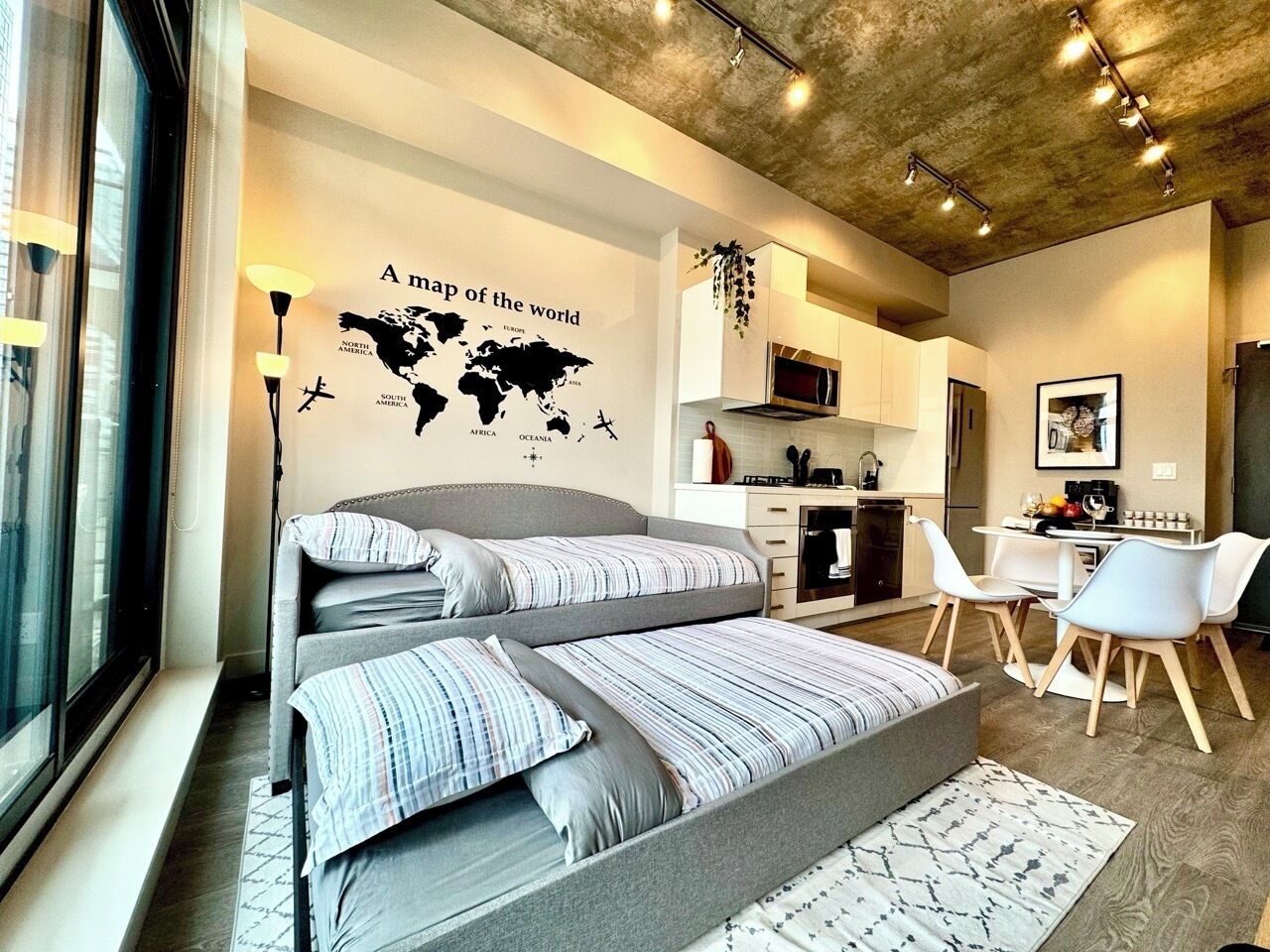 Un dormitorio moderno con un mural de un mapa del mundo, una cama individual superpuesta, un escritorio y una kitchenette.