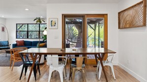 Un coin repas avec une table et des chaises en bois, un canapé bleu et une grande fenêtre donnant sur les arbres.