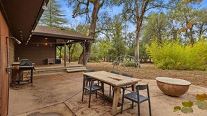 Une terrasse extérieure avec une table et des chaises en bois, un barbecue et un grand bac à fleurs.