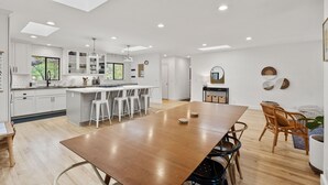 Une cuisine moderne avec des meubles blancs, un îlot central doté de tabourets et des spots encastrés au plafond.