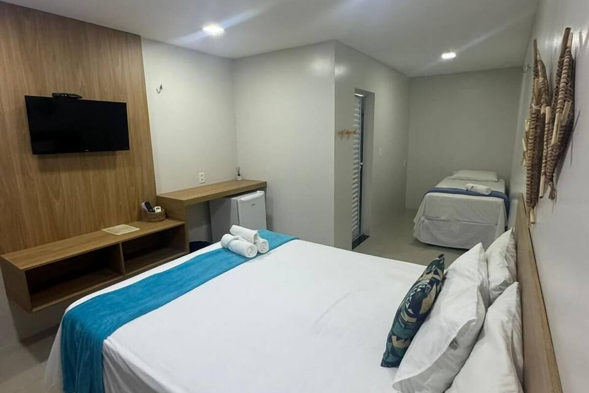 Una habitación de hotel con una cama, un televisor montado en la pared, un escritorio y un armario.