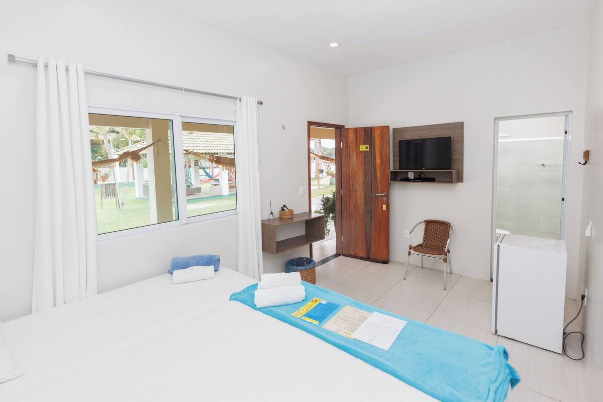 Habitación de hotel con cama, televisor montado en la pared, una pequeña mesa con una silla y una puerta que da a un balcón.