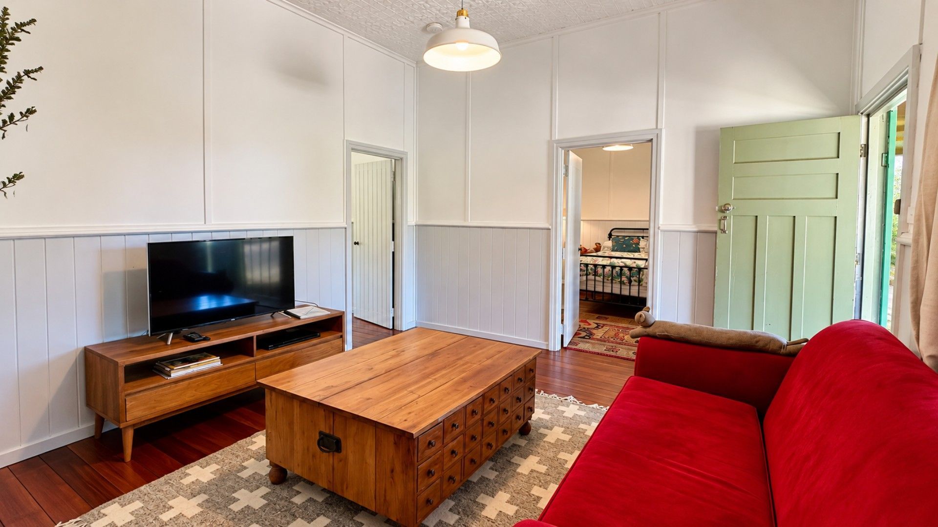 A living room with a television, wooden coffee table, red sofa, and a patterned rug.