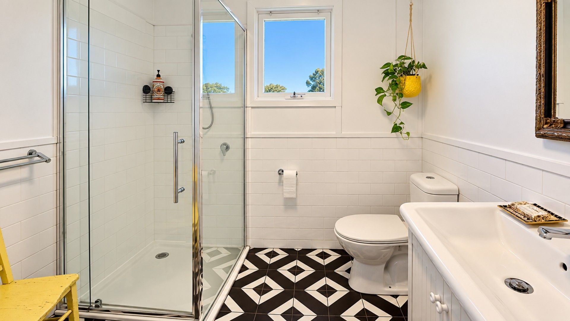 A bathroom with a glass shower enclosure, a toilet, a sink, and a window with a view of trees.