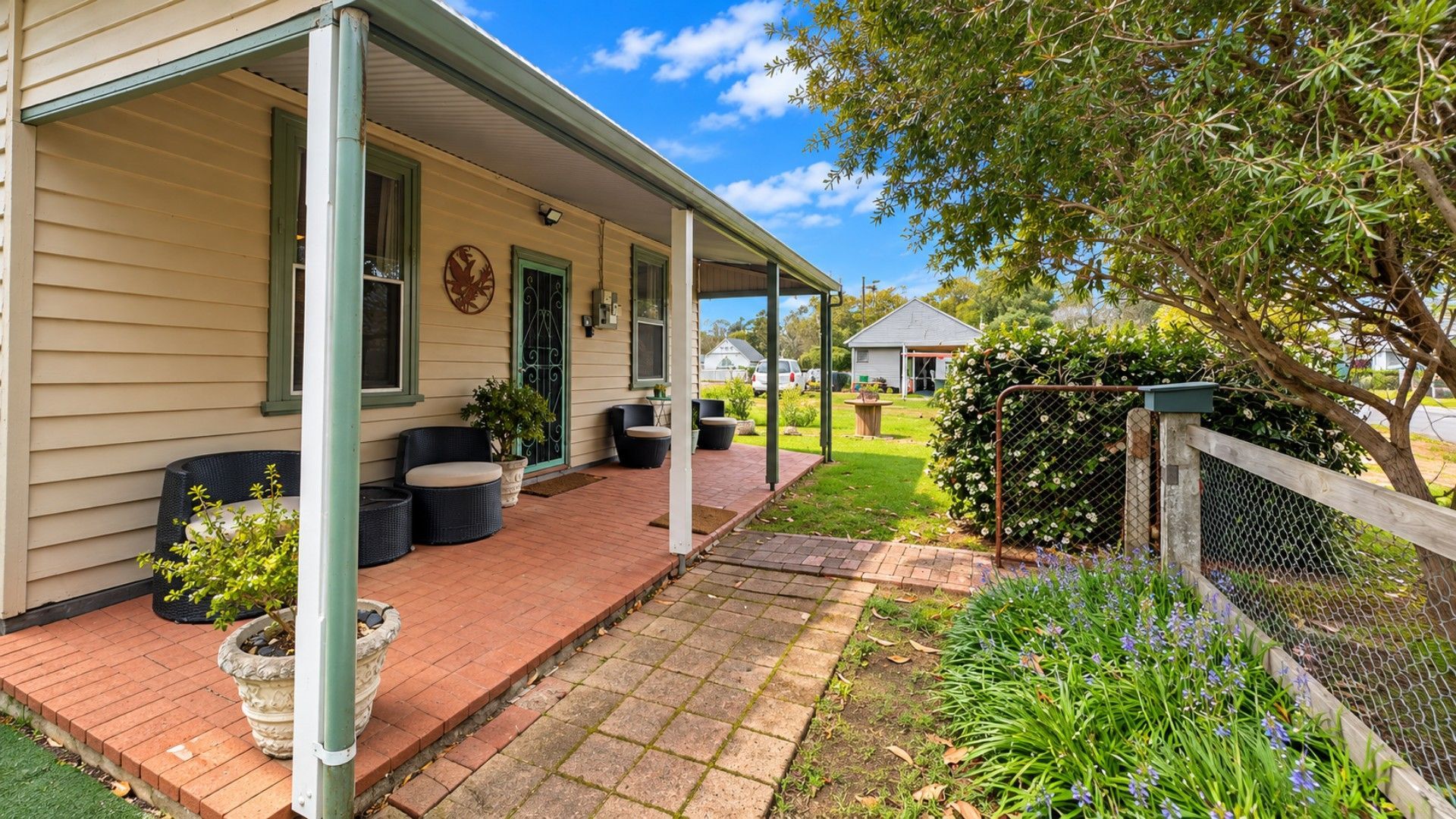 A covered porch with outdoor seating, a fenced garden area, and a small shed in the background.