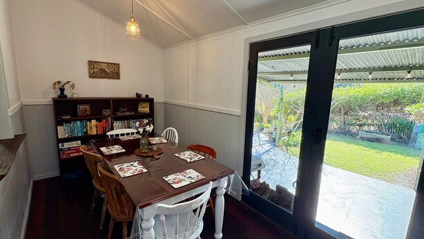 Un comedor con una mesa dispuesta para dos, una estantería y vistas al jardín a través de un ventanal.