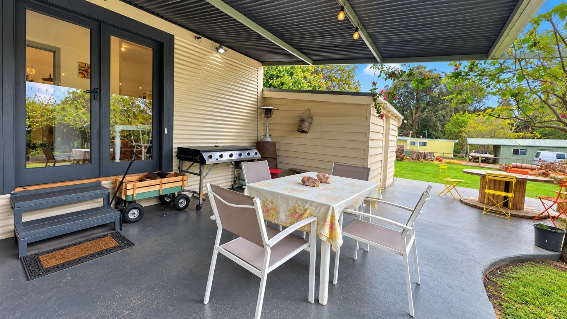 An outdoor patio with a table and chairs, a grill, and a covered area.
