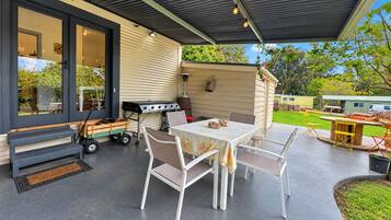 An outdoor patio with a table and chairs, a grill, and a covered area.