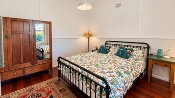 A bedroom with a wooden wardrobe, a bed with floral bedding, a nightstand, and a floor lamp.