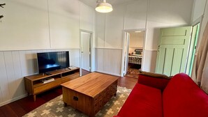 Una sala de estar con una televisión sobre un mueble de madera, un sofá rojo y una mesa de centro de madera.