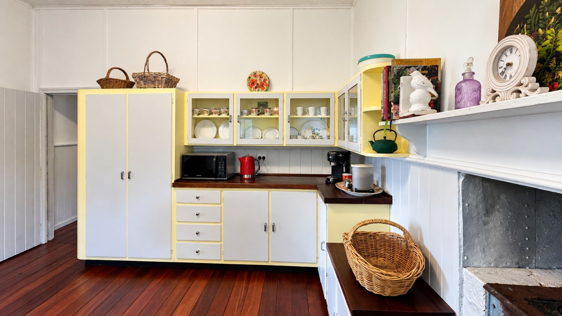 A kitchen with white cabinets, a microwave, a kettle, and a fireplace.