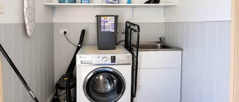 A compact laundry area with a front-loading washing machine, a drying rack, and a small sink.