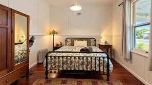 Une chambre à coucher comprenant un lit, une table de chevet, un miroir, un radiateur, une fenêtre avec des rideaux et un ventilateur.