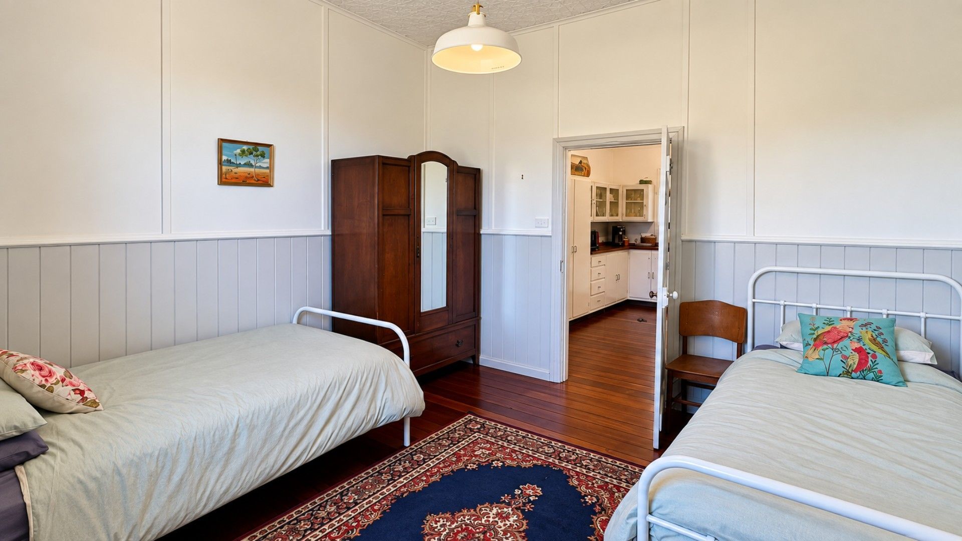 A bedroom with two single beds, a wardrobe, a mirror, and a view into a kitchen area.