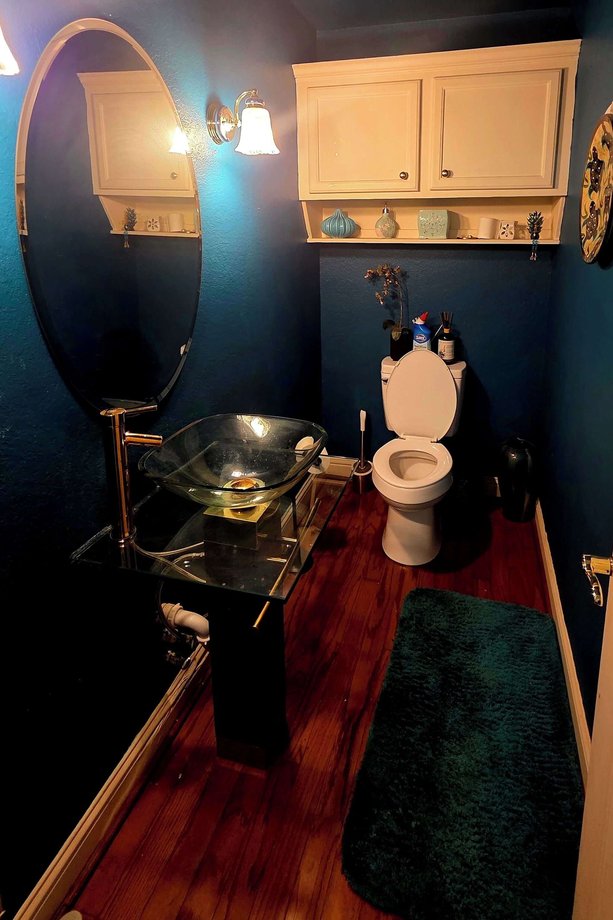 A bathroom with a glass bowl sink, a toilet, a mirror, and a shelf with toiletries.