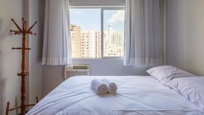 A hotel room with a bed, a wooden coat rack, and a window with curtains.