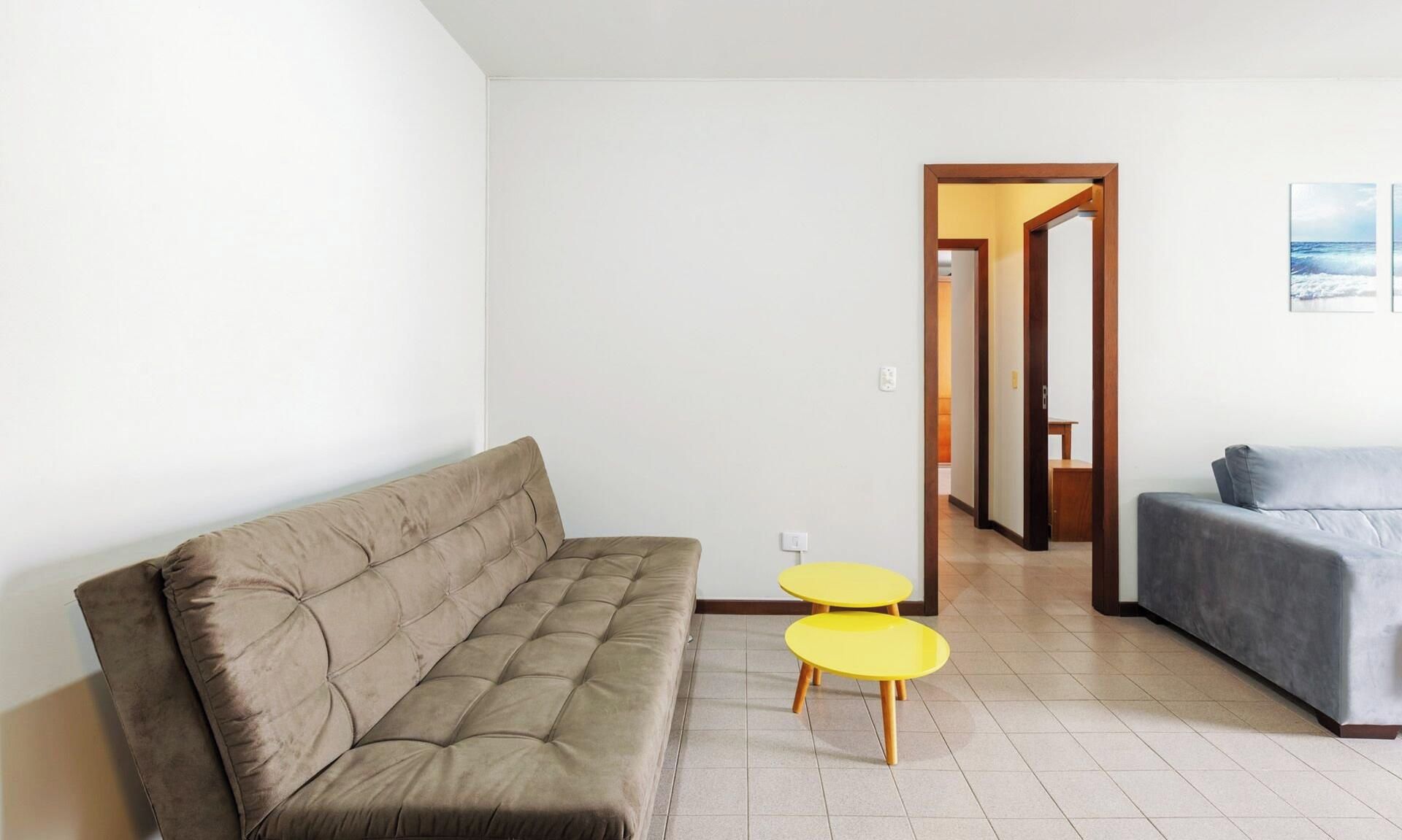 A living room with a sofa, two yellow tables, and a grey couch.