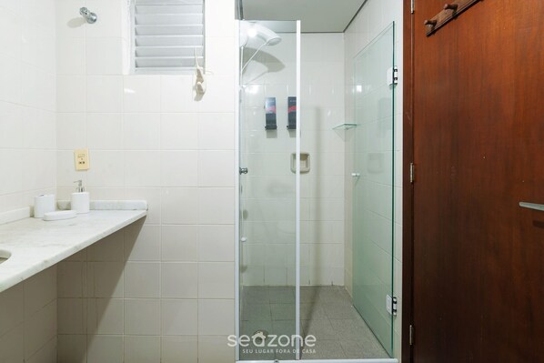 Un baño con cabina de ducha de vidrio, puerta de madera y pared con azulejos blancos.