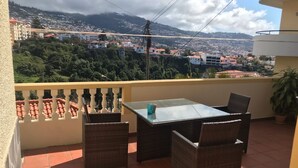 A balcony with a table and chairs, overlooking a cityscape with buildings and greenery. - FUNCHAL TERRACE HOUSE 3BR (Funchal)