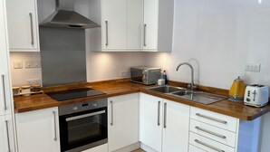 Een moderne keuken met witte kasten, een roestvrijstalen afzuigkap, een inbouwoven, een dubbele spoelbak en een houten aanrecht.
