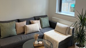 Een moderne woonkamer met een grijze bank, een glazen salontafel en een plant in pot.