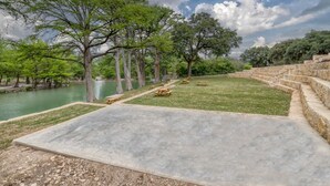 A park with picnic tables, a concrete area, and trees near a body of water. - Bent River Cabin #1 @ Frio River Escape (Concan)