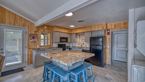 A kitchen with wooden paneling, a central island with stools, a refrigerator, and a microwave. - Bent River Cabin #1 @ Frio River Escape (Concan)