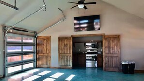 A garage with a large window, a ceiling fan, and a kitchen area with a stove and cabinets. - Bent River Cabin #1 @ Frio River Escape (Concan)