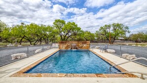 A rectangular swimming pool with a stone border, surrounded by a fence, and trees in the background. - Bent River Cabin #1 @ Frio River Escape (Concan)