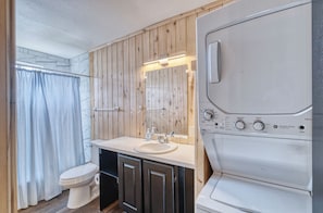 Un baño con tocador de madera, lavabo, inodoro y lavadora.