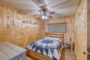 A wooden-paneled room with a bed, a nightstand, a table, and a ceiling fan. - Bent River Cabin #2 @ Frio River Escape (Concan)