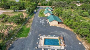 An aerial view of a property with a swimming pool, a fenced area, and a building with a green roof. - Bent River Cabin #5 @ Frio River Escape (Concan)