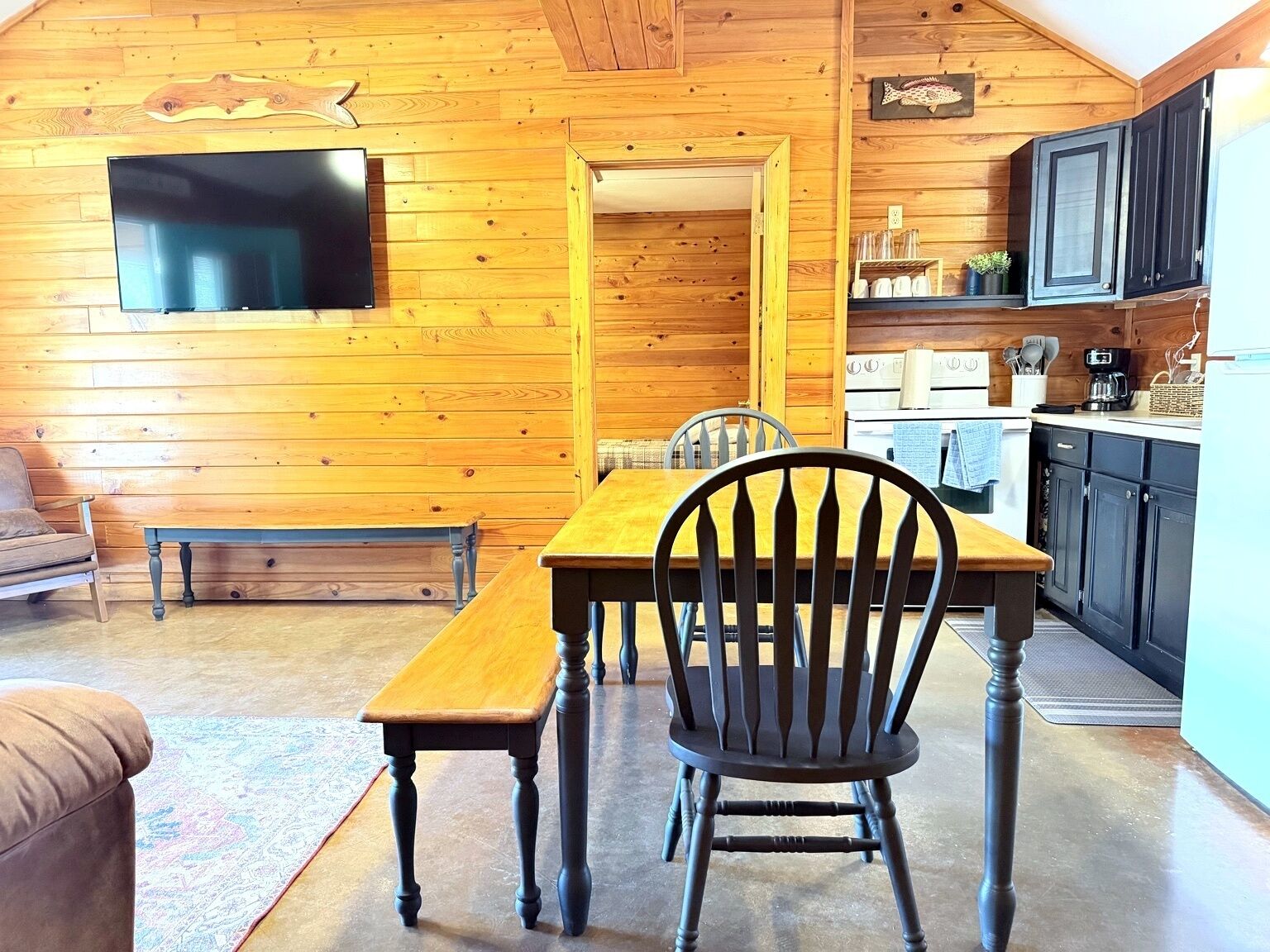 Ein gemütliches Blockhaus-Interieur mit einem Holzesstisch, einer Bank und einem an der Wand montierten Fernseher.