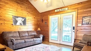 A cozy cabin interior with a leather sofa, a patterned rug, and a wooden dining table. - Bent River Cabin #5 @ Frio River Escape (Concan)