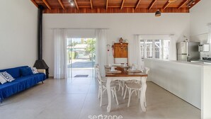 Ένας ευρύχωρος χώρος καθιστικού με ξύλινη οροφή, ένα τραπέζι τραπεζαρίας διαμορφωμένο για τέσσερα άτομα, έναν μπλε καναπέ και μια κουζίνα με ψυγείο και κουζίνα.