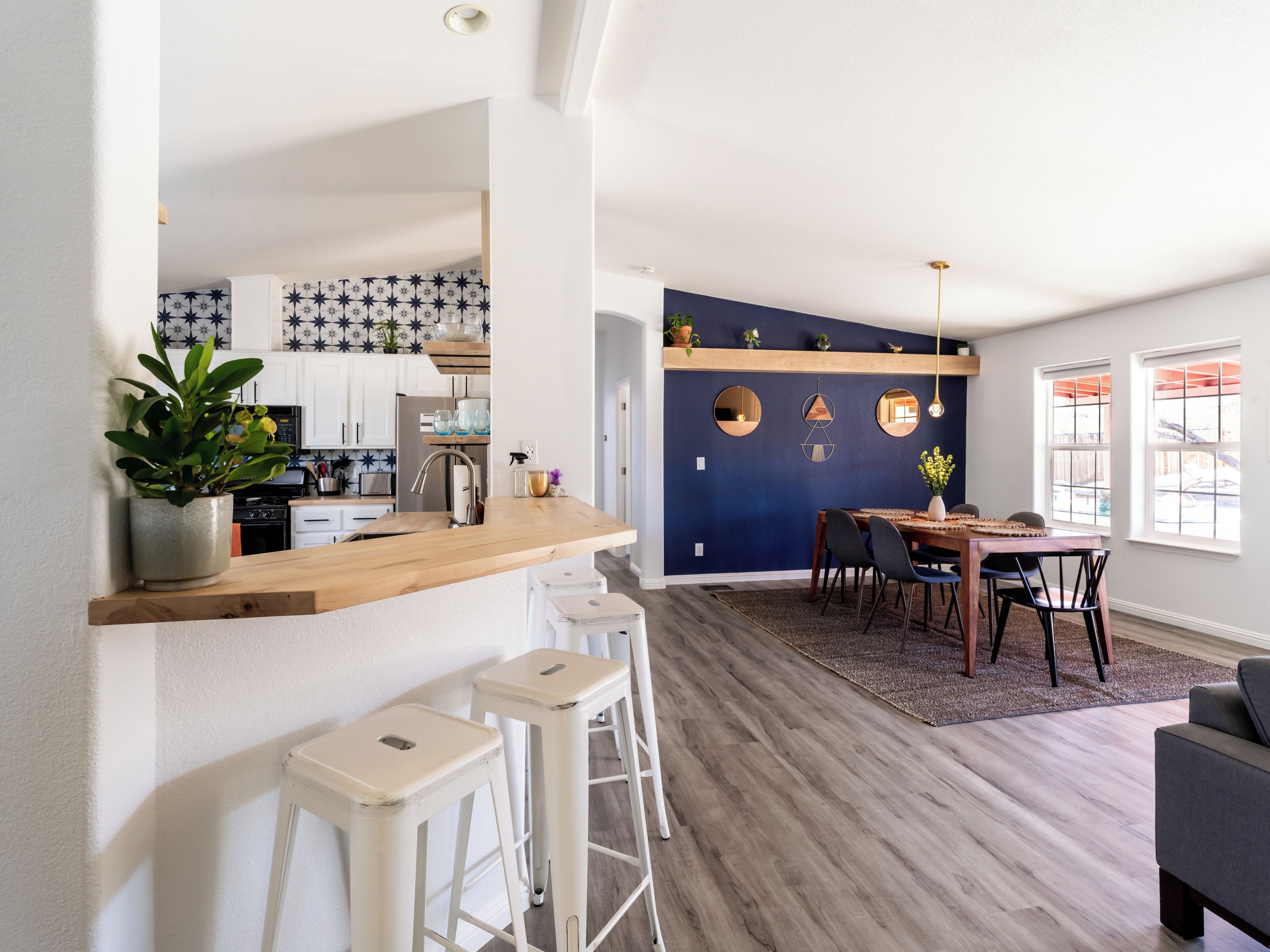 Une cuisine moderne avec des meubles blancs, un plan de travail en bois et un coin repas agrémenté d’un mur bleu foncé et d’une table en bois.