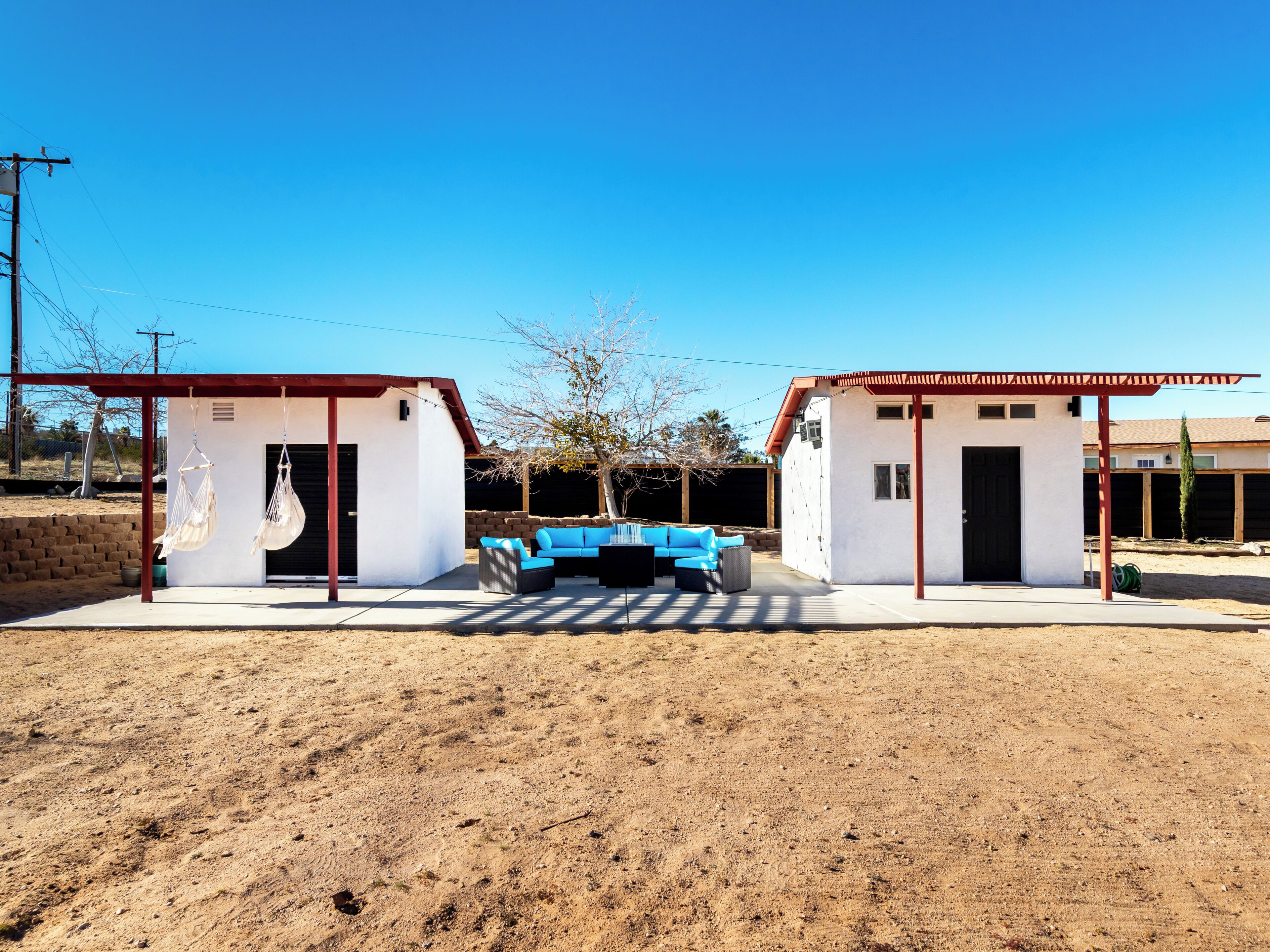 A modern outdoor patio area with a blue sofa, two small structures with red roofs, and a clear blue sky.