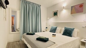 Un dormitorio con una cama grande, una mesita de noche, una lámpara de pared y un ventanal con cortinas.