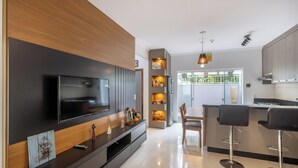 Uma cozinha moderna com TV embutida, painéis de madeira e um espaço de bar com banquetas.