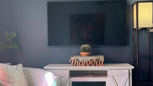 A living room with a fireplace, a flat-screen TV mounted above it, and a 'Thankful' sign on the mantel.