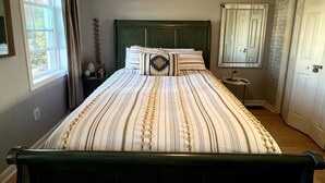 A bedroom with a bed, a nightstand, a window with curtains, a mirror, and a door.