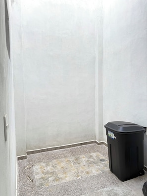 A corner of a room with a tiled floor and a black trash bin. - Encanto de Playa Sur  (Mazatlán)