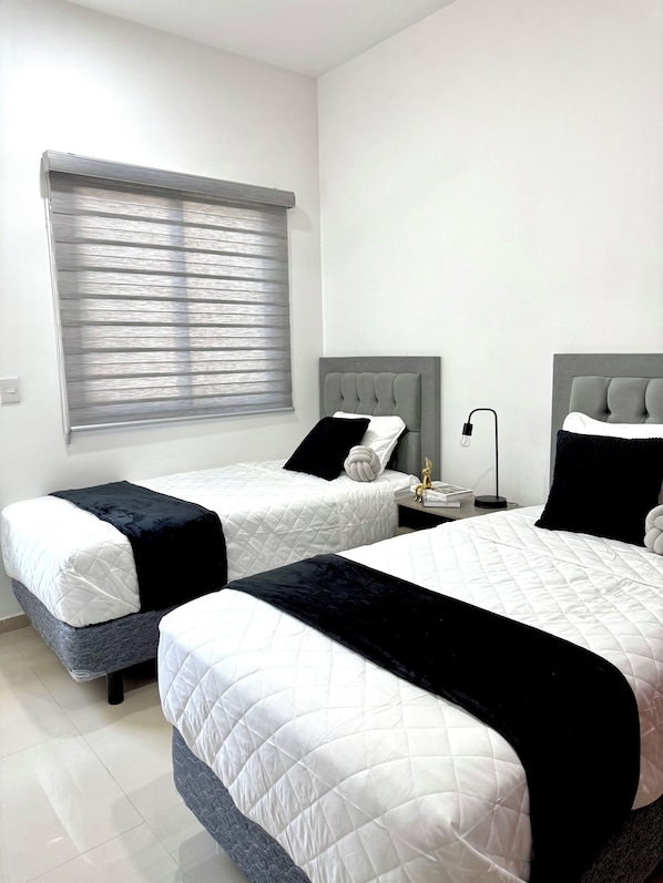 A hotel room with two beds, a window with blinds, a bedside table with a lamp, and a small statue. - Encanto de Playa Sur  (Mazatlán)