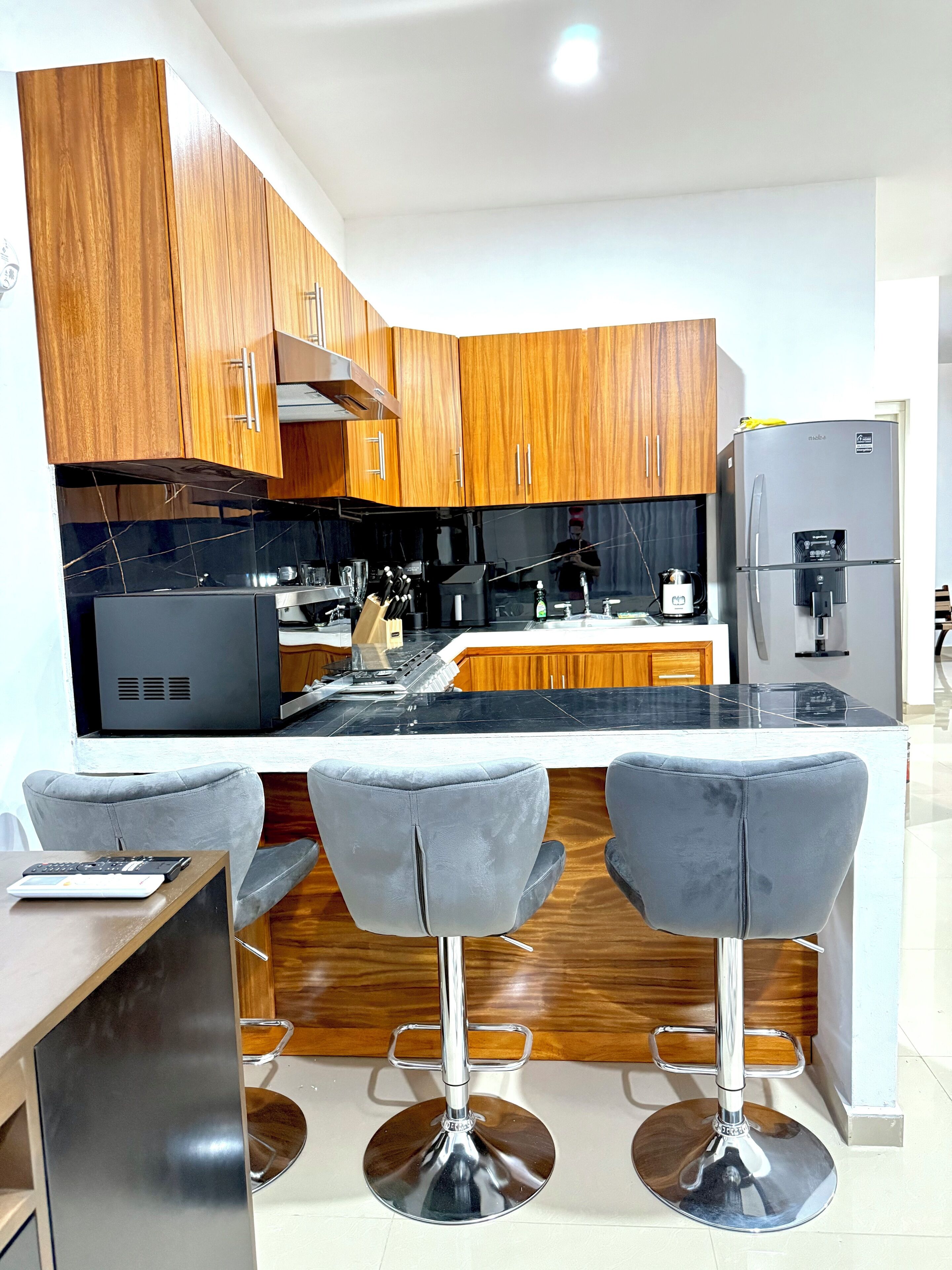 Una cocina moderna con armarios de madera, encimera negra y refrigerador empotrado.