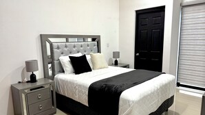 Quarto bem arrumado com cama, mesas de cabeceira e uma porta.