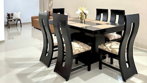 Uma sala de jantar com uma mesa e cadeiras pretas, um ventilador de teto e um vaso com flores sobre a mesa.