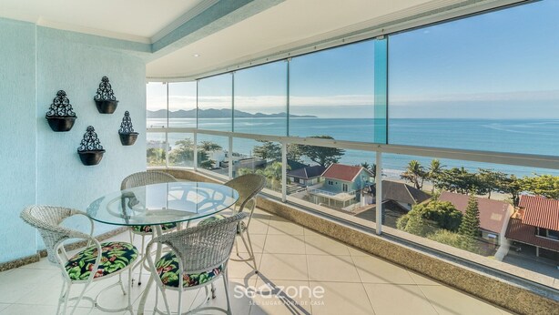 A balcony with a glass table and wicker chairs, overlooking a coastal view with houses and mountains. - Apto 3Qtos Vista Mar a 130m da Praia RDK0801 (Porto Belo)
