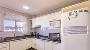 A modern kitchen with white cabinets, a black countertop, a built-in microwave, a stove, and a refrigerator with magnets. - Charming Sea View Apt in Porto Belo Rcs701 (Porto Belo)