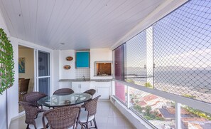 Uma varanda com móveis de vime, uma mesa de vidro e vista para a cidade.