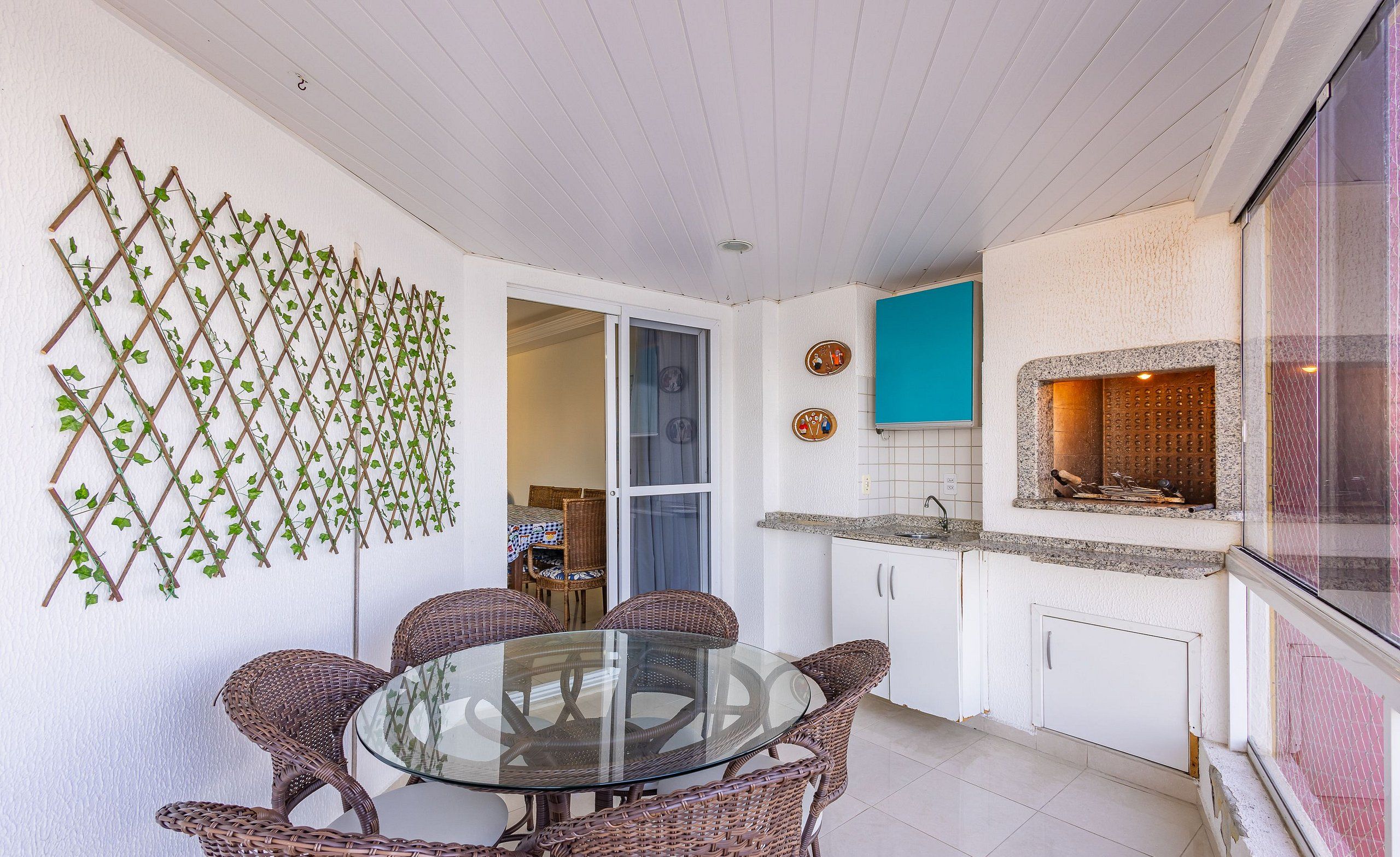 A dining area with wicker chairs and a glass table, a kitchen with white cabinets and a blue accent wall, and a wall-mounted plant trellis.